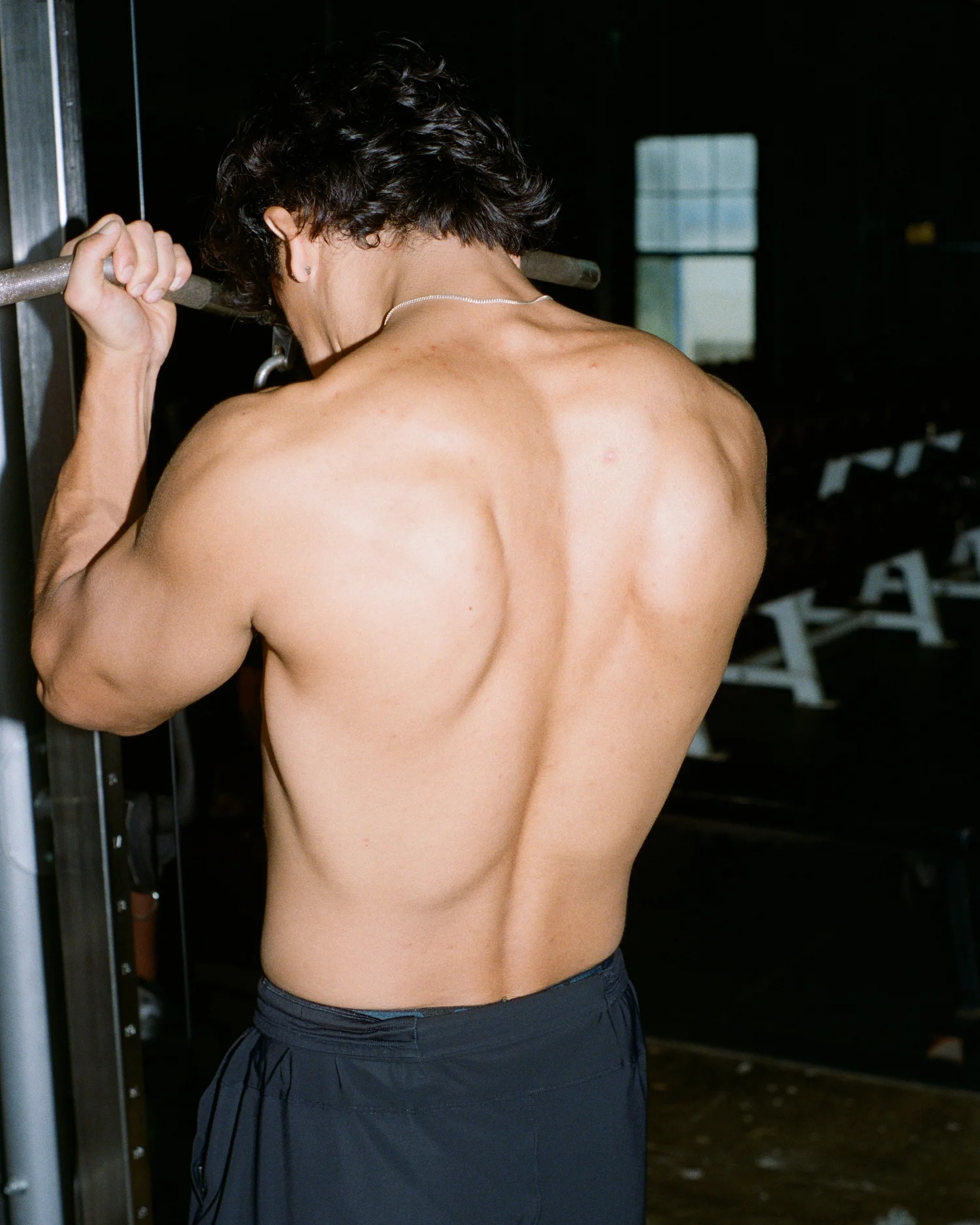 Athlete mid pull-up, photographed from behind in a dark gym — ATX Edit