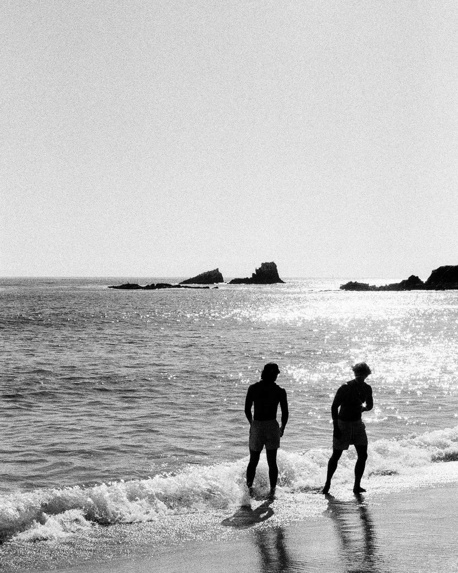 Two figures at the shoreline in black and white