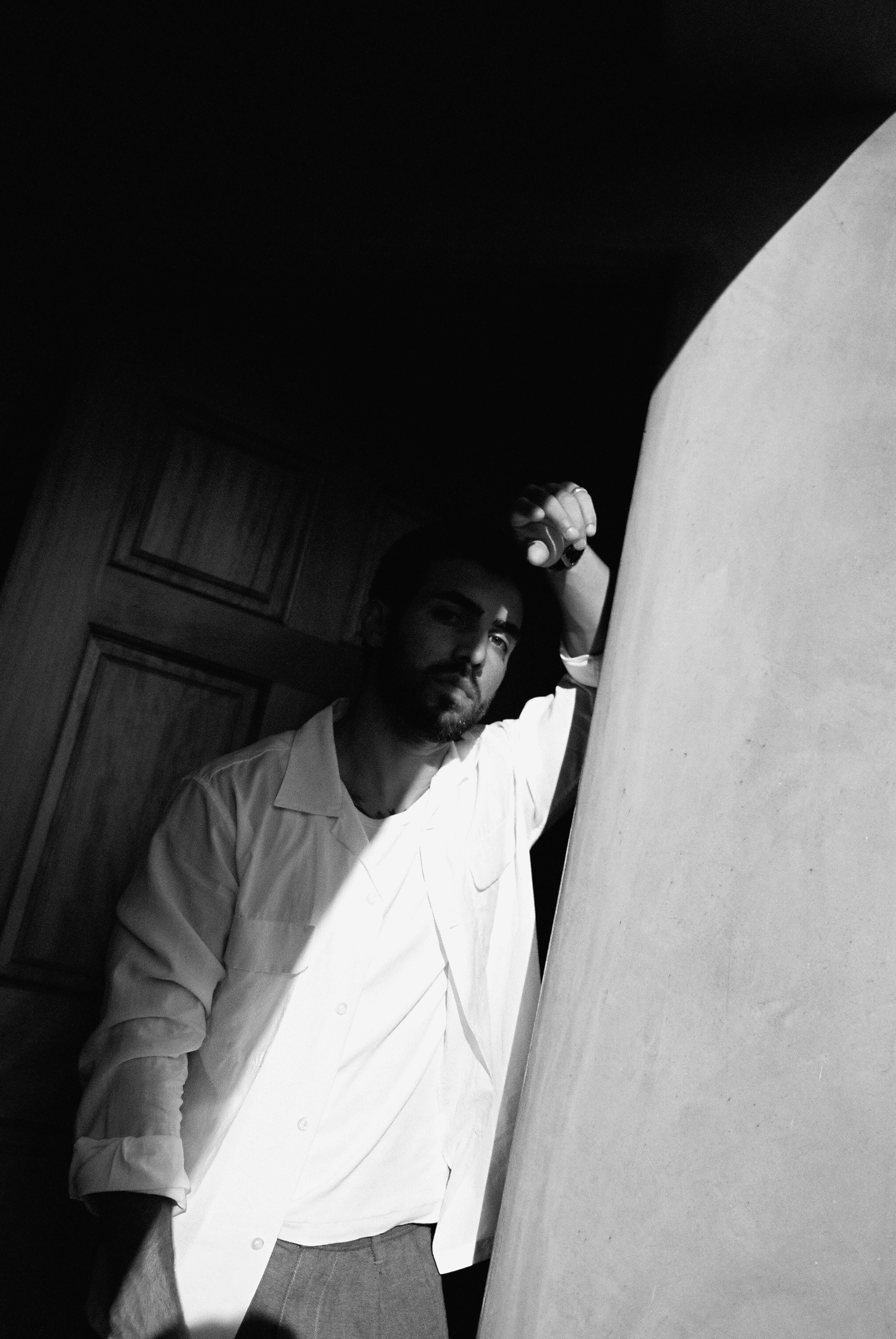 Low-light black and white portrait of Lalo leaning in a doorway